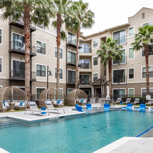 Sparkling swimming pool Resort-style swimming pool with lounge chairs, cabana seating, and palm trees at Hermann Park Lofts in Houston’s Museum District.