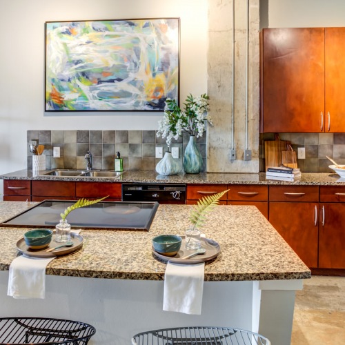 Well-lit kitchen with ample counter space Kitchen with granite countertops, wood cabinetry, breakfast bar seating, and modern appliances at Hermann Park Lofts.